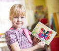 Portrait of cheerful smiling girl holding a bright colorful picture of butterfly painted colors and crayons in kindergarten -