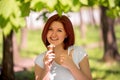 Smiling woman standing under trees in park or forest with big ice-cream and showing thumb up. Enjoying moment and summer leisure