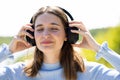 Portrait of a cheerful stylish young millennial woman wearing denim jacket standing outside, listening to music with Royalty Free Stock Photo