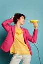 Portrait of cheerful teen girl with curly brown short hair posing with hairdryer isolated over blue background Royalty Free Stock Photo