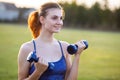 Portrait of cheerful teenage girl in fitness wear exercising with blue dumbbells outdoors in park. Fit young woman working out Royalty Free Stock Photo