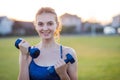 Portrait of cheerful teenage girl in fitness wear exercising with blue dumbbells outdoors in park. Fit young woman working out Royalty Free Stock Photo