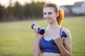 Portrait of cheerful teenage girl in fitness wear exercising with blue dumbbells outdoors in park. Fit young woman working out Royalty Free Stock Photo