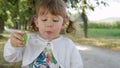 PORTRAIT: Cheerful toddler girl blows soap bubbles on a sunny day in the park. Royalty Free Stock Photo