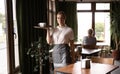 Portrait of cheerful waitress serving on tray cake and cup of beverage in cafe Royalty Free Stock Photo