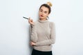 Portrait of Thinking woman with appealing smile, having hair bun in sweater isolated on white background holding pen and have a pe Royalty Free Stock Photo