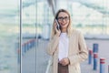 Cheerful woman with glasses blonde holding a mobile phone smiling talking on a smartphone near the office Royalty Free Stock Photo