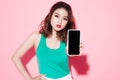 Portrait of a cheerful woman showing blank smartphone screen over pink background. Focus on smartphone Royalty Free Stock Photo