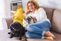 Portrait of cheerful young adult beautiful woman with two dogs pug sitting and relaxing on the sofa at home - concept of animal Royalty Free Stock Photo