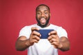 Portrait of a cheerful young african man dressed in casual playing games on mobile phone isolated over red background Royalty Free Stock Photo