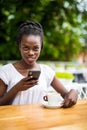 Portrait of cheerful young african woman sitting at outdoor cafe and tyoing on phone Royalty Free Stock Photo