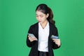 Portrait of cheerful young Asian business woman holding mobile smart phone and credit card on green isolated background Royalty Free Stock Photo