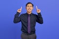 Portrait of cheerful young Asian man pointing up direct ads promotion on purple background Royalty Free Stock Photo