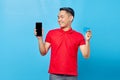 Portrait of cheerful young asian man showing blank screen mobile phone and credit card isolated on blue background