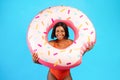 Young black lady in swimsuit posing with donut shaped inflatable ring, smiling at camera over blue studio background Royalty Free Stock Photo