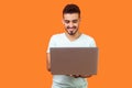 Portrait of cheerful young brunette man typing on laptop, surfing the web. indoor studio shot isolated on orange background Royalty Free Stock Photo