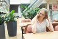 Portrait of a cheerful young caucasian blond business woman sitting on the table, talking at phone, smiling and looking away. Royalty Free Stock Photo