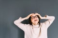 Portrait of cheerful young caucasian woman in eyeglasses holding hands on head on gray background looking on camera Royalty Free Stock Photo