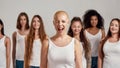 Portrait of cheerful young caucasian woman with shaved head in white shirt winking at camera. Group of diverse women Royalty Free Stock Photo