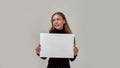 Portrait of cheerful young caucasian woman smiling aside, holding white blank banner in front of her while standing Royalty Free Stock Photo