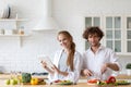 Portrait of a cheerful young couple cooking salad together according to a recipe on a tablet computer, looking at camera Royalty Free Stock Photo