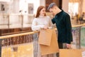 Portrait of cheerful young couple walking shopping mall holding shopping bags, looking inside, excited about their new Royalty Free Stock Photo