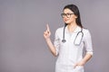 Portrait of cheerful young female doctor with stethoscope over neck looking at camera isolated on grey background. Pointing finger Royalty Free Stock Photo