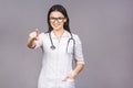 Portrait of cheerful young female doctor with stethoscope over neck looking at camera isolated on grey background. Pointing finger Royalty Free Stock Photo