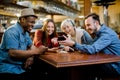 Portrait of cheerful young friends looking at smart phone while sitting in cafe. Mixed race people sitting at a table in Royalty Free Stock Photo