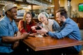 Portrait of cheerful young friends looking at smart phone while sitting in cafe. Mixed race people sitting at a table in Royalty Free Stock Photo