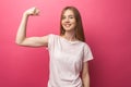 Portrait of cheerful young girl bending biceps on pink background, cute and attractive,