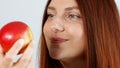 Portrait of cheerful young girl eating red apple on gray wall background. Woman biting ripe fruit. Apple vitamin snack. Royalty Free Stock Photo