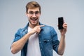 Portrait of a cheerful young man in t-shirt isolated over gray backgound, showing blank screen mobile phone Royalty Free Stock Photo