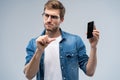 Portrait of a cheerful young man in t-shirt isolated over gray backgound, showing blank screen mobile phone Royalty Free Stock Photo