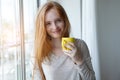 Portrait of cheerful young smiling red hair woman holding yellow coffee cup, enjoying morning coffee and new day Royalty Free Stock Photo