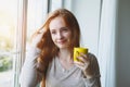 Portrait of cheerful young smiling red hair woman holding yellow coffee cup, enjoying morning coffee and new day, waking up Royalty Free Stock Photo