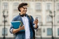 Portrait of cheerful young student guy with smartphone and workbooks posing outdoors Royalty Free Stock Photo