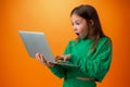 Portrait of a cheerful young teen girl holding laptop computer against orange background Royalty Free Stock Photo