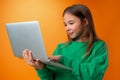 Portrait of a cheerful young teen girl holding laptop computer against orange background Royalty Free Stock Photo