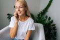 Portrait of cheerful young woman with blonde hair talking on mobile phone at home. Smiling female making answering call Royalty Free Stock Photo