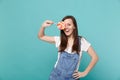 Portrait of cheerful young woman in denim clothes holding, covering eye with colorful round lollipop isolated on blue Royalty Free Stock Photo