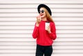 Portrait cheerful young woman eating sweet donut and holding coffee cup on city street white wall