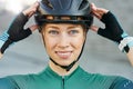 Portrait of cheerful young woman, female cyclist putting on biking helmet, smiling at camera while posing outdoors on a Royalty Free Stock Photo