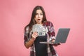 Portrait of a cheerful young woman holding money banknotes and celebrating isolated over pink background. Using laptop Royalty Free Stock Photo