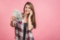 Portrait of a cheerful young woman holding money banknotes and celebrating isolated over pink background. Using mobile phone Royalty Free Stock Photo