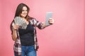 Portrait of a cheerful young woman holding money banknotes and celebrating isolated over pink background. Using tablet Royalty Free Stock Photo