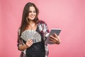 Portrait of a cheerful young woman holding money banknotes and celebrating isolated over pink background. Using tablet Royalty Free Stock Photo