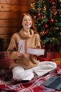 Portrait of cheerful young woman opening gift box with Christmas present on background of xmas tree Royalty Free Stock Photo