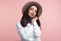 Portrait of cheerful young woman wearing light brown hat and white shirt smiling happily while posing in studio over pink wall Royalty Free Stock Photo