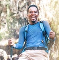 Portrait of a cheerfully laughing African-American Ethnicity young man sitting with a backpack and trekking poles and resting in